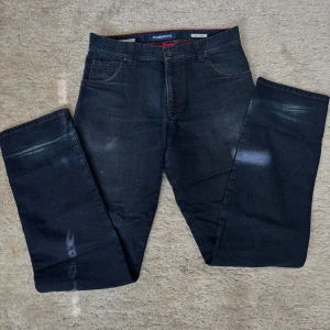 Mörkblå jeansbyxor från Alberto - Säljer ett par mörkblå jeansbyxor från Alberto i modellen Modern Fit. Byxorna har klassisk femficksdesign, röda sömmar på insidan och subtila slitningar framtill. Tillverkade i bomull med lite elastan för extra komfort.
