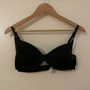 Svart spets-bh  - Säljer en svart bh från H&M med fina spetsdetaljer och liten rosett framtill. Bh:n har justerbara axelband och hakknäppning bak. Perfekt för dig som gillar en klassisk och stilren look med lite extra detaljer. obs: jag använder inte denna pga jag tycker att den sotter ”löst”
