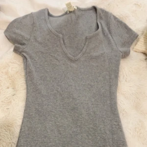 Grå ribbad kortärmad klänning från Bozzolo - Grå ribbad klänning från Bozzolo i mjuk bomullsblandning. Klänningen har korta ärmar och en snygg v-ringning. Perfekt för dig som gillar en enkel och stilren look.