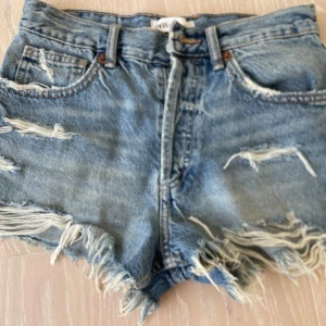 Blå jeansshorts med lite snygga slitningar - Säljer ett par blå jätte snygga  jeansshorts från Zara med råa kanter och tydliga slitningar framtill och baktill. Shortsen har fem fickor  och klassisk dragkedja med knapp. Pris kan diskuteras. Perfekta för sommaren!