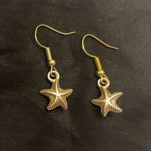 Guldiga örhängen med sjöstjärnor boho  - Säljer ett par snygga örhängen i guld imitation med hängande sjöstjärnor. Ca  0,7 x 0,7 cm. 