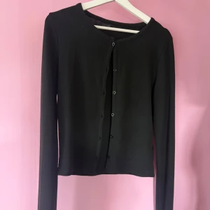Svart kofta med knappar - En enkel och stilren svart kofta med långa ärmar och knäppning framtill. Perfekt att slänga över en topp eller klänning för en snygg lager-på-lager-look. Använd 1 gång.