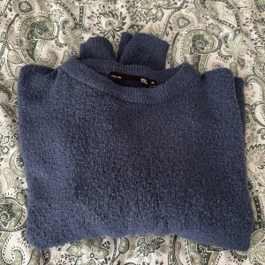 Blå stickad tröja från lager 157 - Mysig blå stickad tröja från lager 157 i storlek M. Tröjan har en rund halsringning och är tillverkad i ett mjukt, strukturerat material som känns skönt mot huden. Perfekt för kyligare dagar.