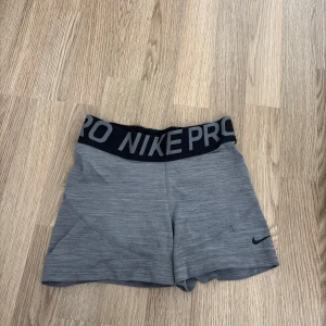 Grå träningsshorts från Nike Pro - Snygga grå träningsshorts/ hotpantsfrån Nike Pro med svart resår i midjan där det står 'NIKE PRO' i vitt. Shortsen har en tight passform och är perfekta för gym eller löpning. Liten svart Nike-logga på ena benet. Strorlek XS🩷100kr