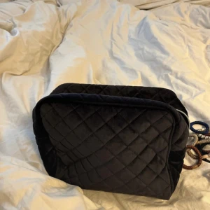 Svart stor quiltad necessär - Säljer en svart stor quiltad necessär med dragkedja. Väskan är mjuk och har ett rymligt fack invändigt, perfekt för att organisera smink eller småprylar. Klassisk och stilren design som passar i alla väskor.
