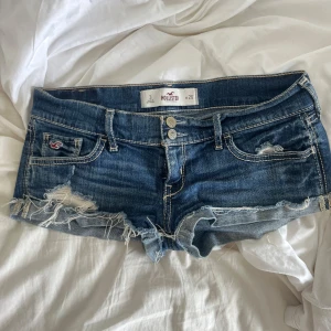 Blå jeansshorts från Hollister - Snygga blå lågmidjade jeansshorts från Hollister med fransade kanter och slitningar framtill. Storlek 26, passar mig som brukar ha S🥰🫶🏼