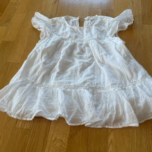 Vit volangtopp med spetsdetaljer - Söt vit topp med volanger och spetsdetaljer. Toppen har korta ärmar och en luftig, flowy passform. Perfekt för varma dagar och har en romantisk känsla med sina fina detaljer.