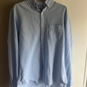 Ljusblå skjorta från Dressmann - Säljer en ljusblå skjorta från Dressmann i slim fit-modell. Skjortan har klassisk krage med knappar, bröstficka och långa ärmar. Perfekt för en stilren look och enkel att matcha med olika outfits.