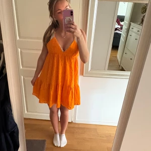 Orange ärmlös klänning med volang - Säljer en superfin orange kortklänning med v-ringning och volang nertill. Klänningen är ärmlös och har en luftig passform, perfekt för varma dagar. Snygg att styla med sneakers eller sandaler!