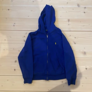 Blå hoodie från Ralph Lauren - Säljer en blå hoodie från Ralph Lauren med dragkedja och huva. Klassisk gul broderad logga på bröstet. Skicka om ni undrar något!