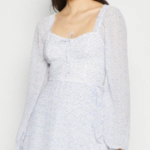 Hollister Klänning  - Supersöt vit/blå kortklänning från Hollister med små blå blommor, långa puffärmar och volangdetaljer. Klänningen har omlottmodell och knyt framtill vid bysten. Perfekt för sommaren och skolavslutningar osv! Köpt på Zalando för 566kr men bara använd en gång, har tyvärr inte förpackning kvar. Kom privat för fler frågor💞