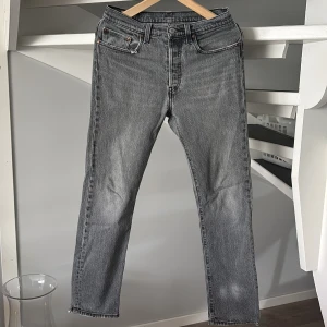 Grå jeansbyxor Levis 501  - Säljer ett par grå Levi's 501 jeans. Byxorna har normal passform. Dem är i bra skick förutom att det är en liten missfärgning nere på vänster ben som du kan se på första bilden, men annars ett par super fina jeans som passar till allt. Bara att höra av dig om du undrar över något 