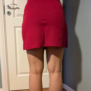 Röd minikjol från Bershka - Säljer en snygg röd minikjol från Bershka. Kjolen har en enkel och stilren design med lätt utsvängd form och dragkedja bak. Perfekt att matcha med en crop top eller stickad tröja.