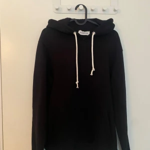 Svart hoodie från pier one - Säljer en svart hoodie från pier one med vit dragsko i huvan. Klassisk modell med lång ärm och mjukt material, perfekt för en avslappnad stil.