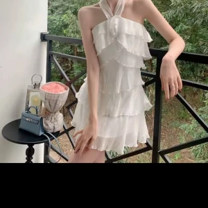 Vit volangklänning med halterneck - Supersöt vit kortklänning med flera lager volanger och halterneck-knäppning. Klänningen har en luftig känsla och är perfekt för varma dagar. Materialet är lätt och ger en romantisk look.