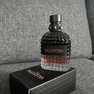 Valentino parfymflaska med nitar - Säljer en lyxig parfym från Valentino i en cool glasflaska med nitar och svart etikett. Flaskan har en gradient från svart till transparent och rymmer en bärnstensfärgad vätska. Kommer med originalkartong och har en snygg, modern design.