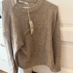 Beige stickad tröja från NA-KD - Mysig beige stickad tröja från NA-KD med rund halsringning och breda ribbade muddar vid ärmslut och nederkant. Perfekt för lager-på-lager och enkel att matcha med jeans eller kjol.