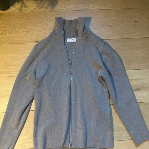 Fullzip från Ljung  - Säljer en beige ribbad kofta från Ljung i storlek M. Tröjan har hel dragkedja framtill, hög krage och långa ärmar. Perfekt för lager-på-lager och enkel att matcha med olika outfits. Nypris ligger på 1500. 