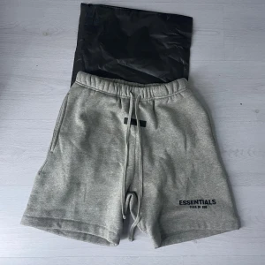 Grå shorts från Essentials Fear of God - Snygga grå shorts från Essentials Fear of God med broderad logga på vänster ben. De har elastisk midja med snörning och sidofickor. Perfekta för en avslappnad stil. 🙌