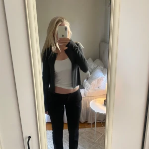 Mörkgrå croppad kofta - Säljer en mörkgrå croppad kofta med lång ärm. Enkel och stilren design med en knapp upptill och öppen framtill. Perfekt att slänga över ett linne eller t-shirt för en avslappnad look.