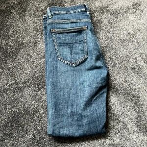 Blå raka jeans - Klassiska blå jeans med raka ben och femficksdesign. Jeansen har kontrastsömmar och normal passform, perfekta till vardags. Tillverkade i denim med en snygg tvättad look tiger of Sweden jeans perfekt skick