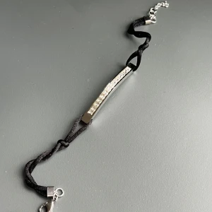 Svart armband med silverfärgad detalj och glittriga stenar - Helt nytt armband från Lois Lane – ett svenskt varumärke som gör stilrena smycken i hållbara material. Armbandet har svart silkesband och en skinande bricka i nickelsäkert kirurgiskt stål (316L), dekorerad med små gnistrande stenar. Justerbar längd ca 21–23 cm. Butikspris 400 kronor.   Ingen prutning – men jag erbjuder rabatt vid köp av flera saker. Jag rensar smyckesskrin och garderob, så kika gärna på mina andra annonser också!  