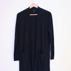 Lång svart kofta Lindex strl S - Lång svart öppen kofta från Lindex strl S, har två fickor, slutar precis under knäna på mig som är 165cm. Mått: längd från axel 110, bredd 49cm, ärmlängd från axel 63cm. Originalpris 499kr. Kan fixa fler bilder och mått vid intresse! 