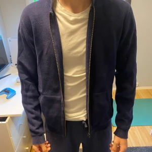 Mörkblå zip-jacka från Oxford - Säljer en mörkblå jacka från Oxford i 100% bomull. Jackan har dragkedja framtill, två fickor och ribbade muddar vid ärmslut och nederkant. Enkel och stilren modell som passar till många tillfällen.