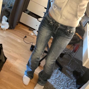 Blå jeansbyxor med broderade bakfickor - Säljer ett par blå jeans från Miss Me med snygga slitningar och broderade detaljer på bakfickorna. Byxorna är mid rise och bootcut. Perfekta för dig som gillar en unik och cool stil.