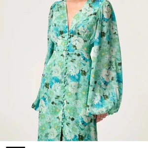 Adore klänning  - Säljer en vacker långklänning i gröna och blå toner med blommigt mönster. Klänningen har v-ringning, långa puffärmar och knappar framtill. Perfekt för dig som vill sticka ut med en färgstark och romantisk look.