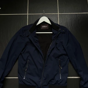 Mörkblå vindjacka från Oscar Jacobson - Riktigt stilig mörkblå vindjacka från Oscar Jacobson. Nypris 3000kr storlek S.