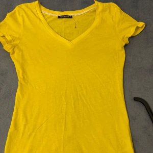 Gul t-shirt med v-ringning från Terranova - Säljer en enkel och fräsch gul t-shirt från Terranova i storlek S. T-shirten har v-ringad hals och korta ärmar, perfekt för varma dagar. Tillverkad i mjuk bomull som känns skön mot huden.