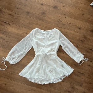 Vit omlottklänning / studentklänning - Säljer en söt vit omlottklänning med knytband i midjan och volangdetaljer. Från ett australienskt märke. Storlek 12 passade mig med 38/40! 🌸🌸🌸  Använd en gång! Slutar vid låren. Har sytt några stygn vid bysten vilket går att sprätta upp om man vill! Perfekt studentklänning eller till sommaren:)  Tog adoore då märker inte hittas:) selfie leslie