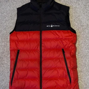 Röd och svart dunväst från Sail Racing - Snygg röd och svart dunväst från Sail Racing med dragkedja framtill. 