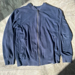 Mörkblå bomberjacka från Hampton Republic - Säljer en stilren mörkblå bomberjacka från Hampton Republic. Jackan har dragkedja framtill och ribbade muddar vid ärmslut och nederkant. Perfekt för en avslappnad look.