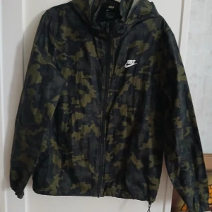 Camouflage vindjacka från Nike. Stl S - Säljer en cool camouflage vindjacka från Nike. Jackan har en dragkedja framtill och en huva för extra skydd. Perfekt för utomhusaktiviteter och har en klassisk Nike-logga på bröstet. Stl.S
