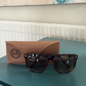 Bruna solglasögon från Ray-Ban - Snygga bruna solglasögon från Ray-Ban med klassisk design. De har en robust båge och mörka linser som ger ett stilrent intryck. Perfekt accessoar för soliga dagar. Levereras med ett brunt fodral för säker förvaring.