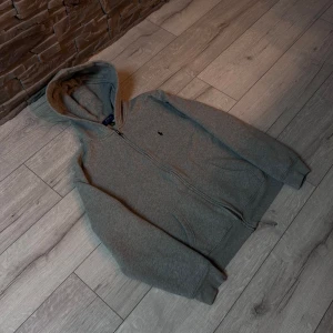 Grå hoodie från Ralph Lauren - Säljer en stilren grå hoodie från Ralph Lauren med dragkedja och huva. Perfekt för en avslappnad look. Den har en liten broderad logga på bröstet och är tillverkad i mjukt material för extra komfort.