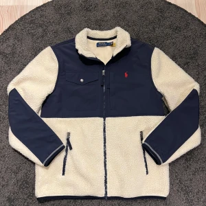 Vit och marinblå fleecejacka från Polo Ralph Lauren - Säljer en snygg vit och marinblå fleecejacka från Polo Ralph Lauren. Jackan är knappt använd och är därav i nyskick. Perfekt inför våren och sommarkvällar! Storlek M och sitter som vanligt. 