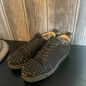 Gråa loubs - Säljer då mina loubs då dom inte användas längre tyvärr är lite grå färg. Borta på vissa nitar med går att måla dom med en penna några spikar saknas kan fås med 3 st. Snygga svarta sneakers med nitar på tån och röd sula. Skorna har snörning och är tillverkade i mocka. Perfekta för att ge din outfit en edgy touch.