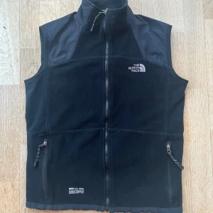 The North Face väst - Svart The North Face väst i fleece/nylon. Den är i bra skick utan defekter (8/10). Den är perfekt att ha över en tjocktröja eller en T-shirt. Hör av dig om du har några frågor eller funderingar.