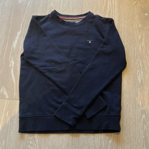Mörkblå sweatshirt från GANT - Säljer en stilren mörkblå sweatshirt från GANT. Tröjan har långa ärmar och en rund halsringning med en diskret logga på bröstet. Perfekt för en avslappnad stil. Passar ungdomar i storlek 158/164 cm. Tröjan är i fint skick 9/10, använd bara ett par fåtal gånger, tveka inte att höra av er⭐️kan gå ner lite i pris🔥