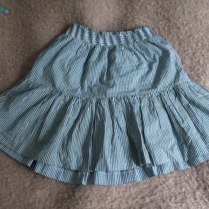 Randig kjol från Ralph Lauren - Säljer en söt randig kjol från Ralph Lauren i blått och vitt. Ser lite gul ut på bild men är ej. Kjolen har en elastisk midja och volangdetaljer som ger en fin form. Perfekt för en sommarlook. 🩵st 10 men någon som är 14 skulle kunna ha den.