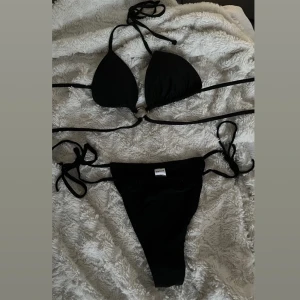 Svart bikini med knytband - Säljer denna svarta bikini med knytband i både över- och underdel. Bikini toppen när även på en guld ring som ger en elegant look. Perfekt för stranden eller poolen. ☀️💞