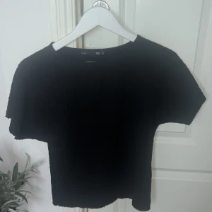 Svart kortärmad topp - Säljer en stilren svart topp med korta ärmar. Perfekt för en enkel och elegant look. Toppen har en normal passform och är tillverkad i ett mjukt material som känns skönt mot huden.