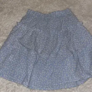 Söt blå kjol med blommigt mönster och volangdetaljer. Perfekt för en somrig look. Kjolen har en bekväm passform och är lätt att matcha med olika toppar.