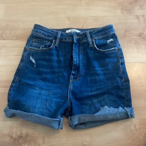 Blå jeansshorts med slitningar - Snygga blå jeansshorts från forever 21 med coola slitningar och uppvikta ben. Perfekta för en avslappnad sommarlook. De har en klassisk femficksdesign och knappgylf.