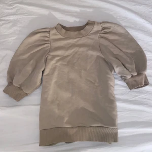 Beige tröja med puffärmar - Säljer en stilren beige tröja med puffiga trekvartsärmar och ribbade muddar. Perfekt för en trendig look. Passar bra till både jeans och kjol.