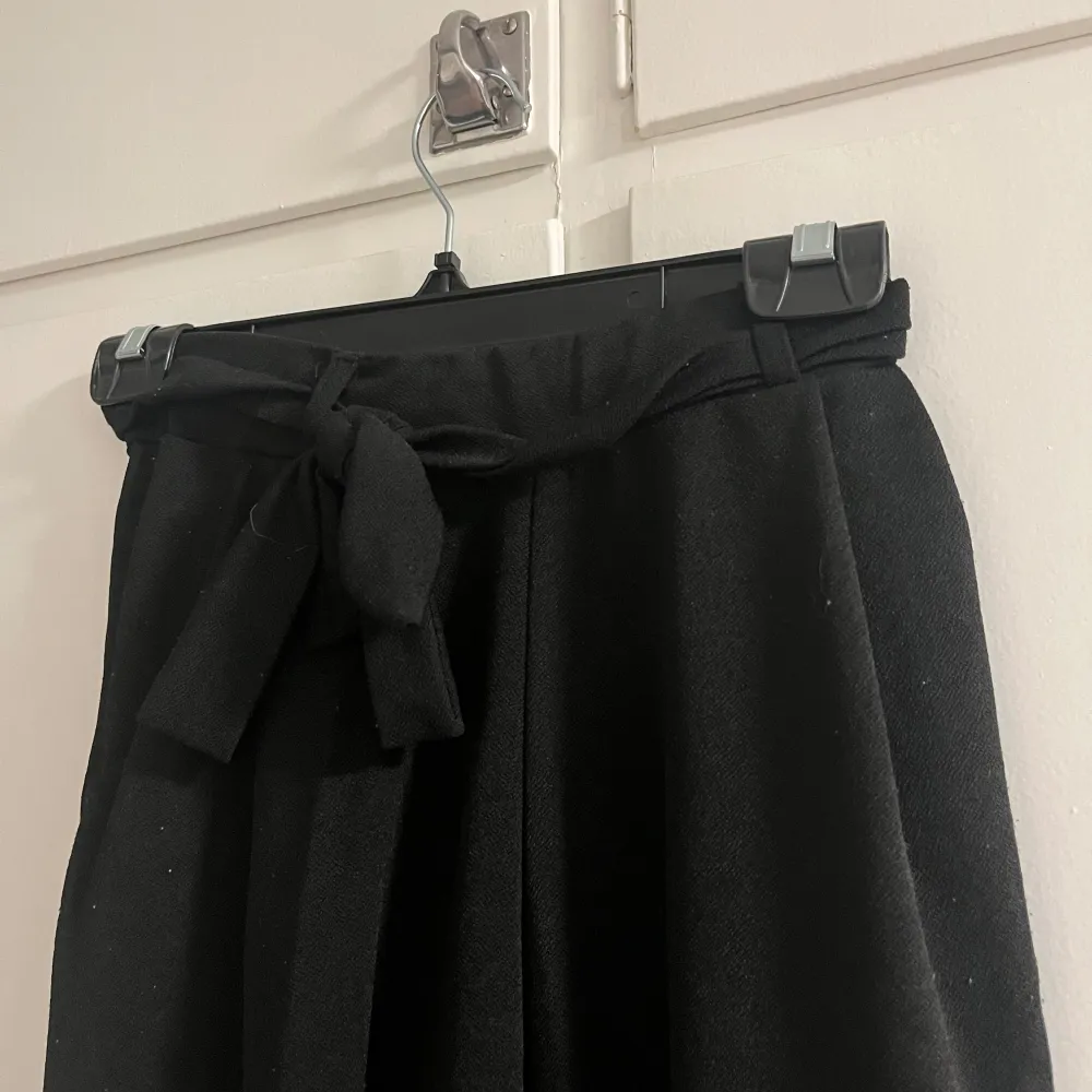 Snygga svarta byxor med hög midja och knytband i midjan. Byxorna har en loose passform och är tillverkade i ett mjukt material som ger en bekväm känsla. De är använda och lite noppriga. Farkut & Housut.