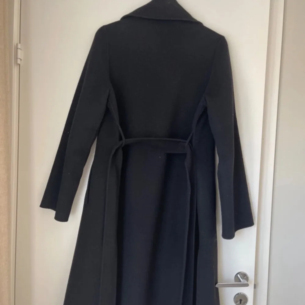 Elegant svart kappa från Zara med klassisk design. Den har långa ärmar och ett bälte i midjan för en stilren look. Perfekt för kyligare dagar.. Takit.